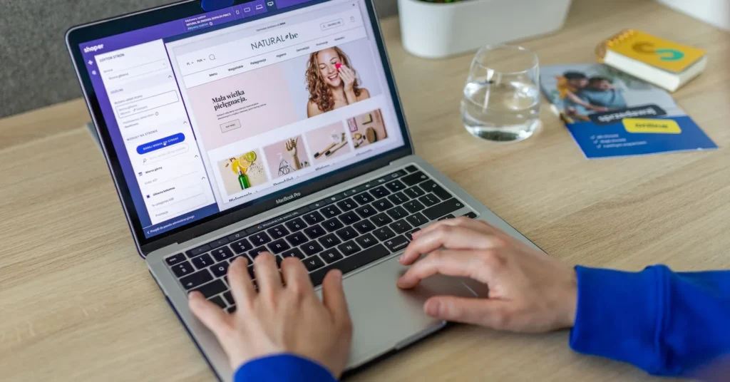 Hands typing on a laptop showing an e-commerce website in a modern office setting